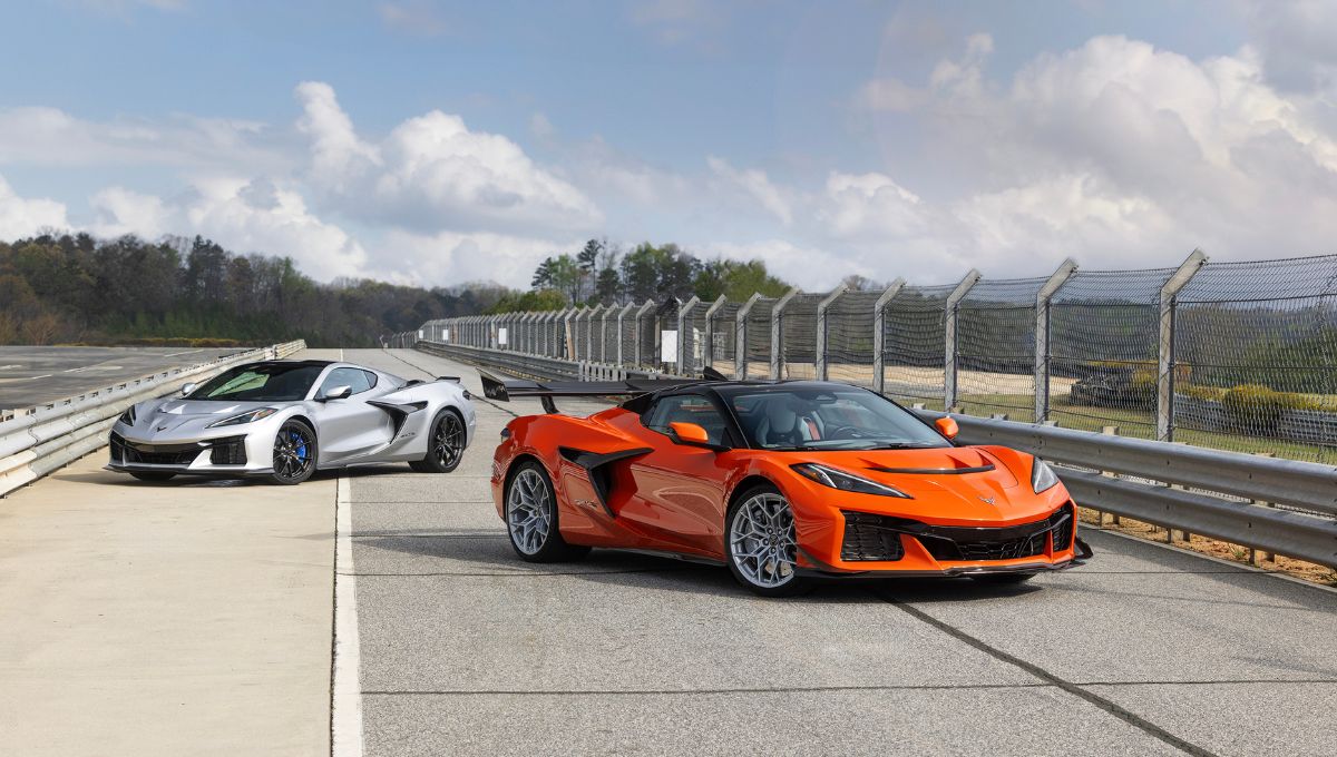 dois Corvettes parados um a frente, e o outra mais para trás. O da frente na cor laranja, e o de trás na cor prata